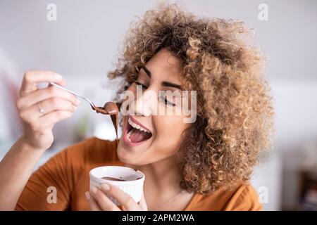 Portrait einer glücklichen Frau, die Schokolade isst, breitete sich zu Hause aus Stockfoto