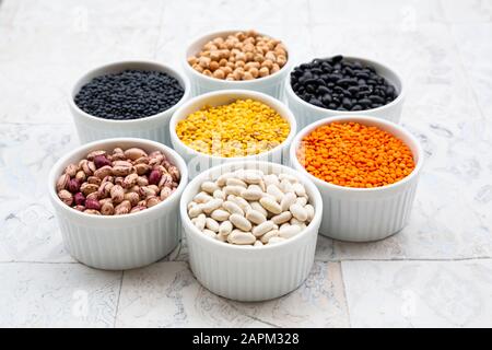 Verschiedene Hülsenfrüchte in Schalen: Kichererbsen, Cannellini Bohnen, Wachtelbohnen, schwarze Bohnen, gelbe Linsen, rote Linsen, schwarze Linsen Stockfoto