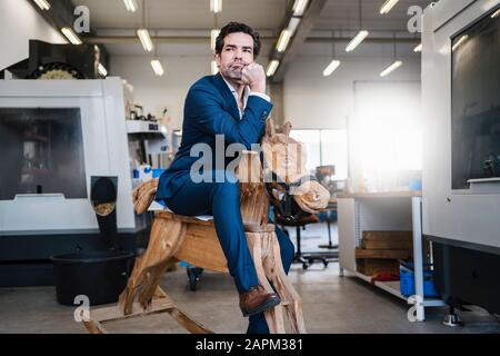 Penibler Geschäftsmann auf Holzrockpferd in einer Fabrik Stockfoto