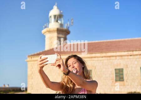 Junge Frau fotografiert den Leuchtturm von Punta Nati auf Menorca, Spanien Stockfoto