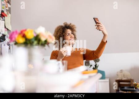 Frau, die eine Tasse Kaffee hält und ein selfie zu Hause nimmt Stockfoto