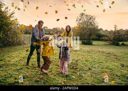 Fröhliche Familie, die mit Herbstlaub auf einer Wiese spielt Stockfoto