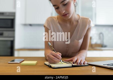 Teenagerin schreibt in ihrem Kalender in der Küche Stockfoto