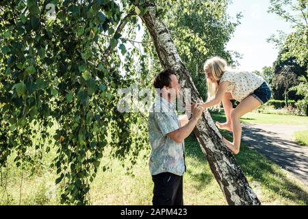 Vater hilft Tochter beim Besteigen eines Birkenstamms im Park Stockfoto