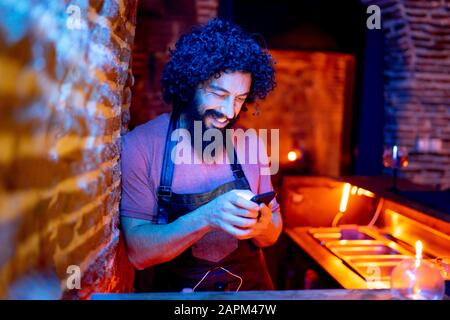 Junger Mann, der in der Bar arbeitet und Smartphone verwendet Stockfoto