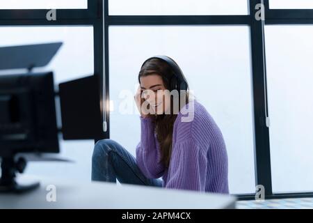 Porträt einer lächelnden jungen Frau, die mit Kopfhörern in einem Studio sitzt Stockfoto