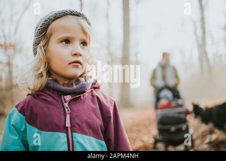 Blondes Mädchen mit Mutter, Schwester und Grenzkollie im Hintergrund beim Waldspaziergang im Herbst Stockfoto