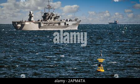 Eine gelbe Boje befindet sich in der Tokioter Bucht vor der Küste von Yokosuka, Japan, mit einem Schiff der US Navy, das auf See aufgeht. Stockfoto