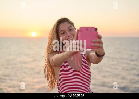 Junge Frau fotografiert bei Sonnenuntergang am Meer von sich Stockfoto