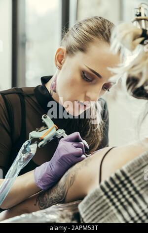 Tätooistische Frauen, die den Oberarm der weiblichen Kundin tätowieren Stockfoto