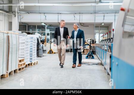 Zwei Geschäftsleute, die in einer Fabrik spazieren und reden Stockfoto