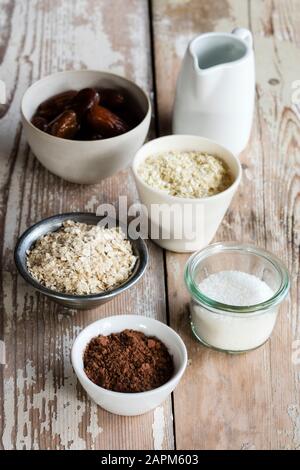 Zutaten für die Herstellung von Eiweißbällchen (Kokosöl, Datteln, Hirseflocken, Haferflocken, geriebene Kokosnuss und Kakaopulver) Stockfoto