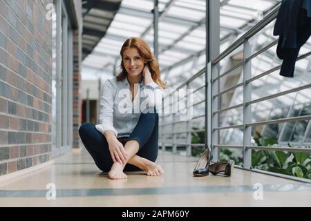 Porträt einer lächelnden Geschäftsfrau, die in einem modernen Büro auf dem Boden sitzt Stockfoto