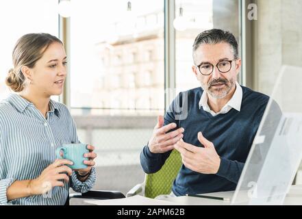 Reifer Geschäftsmann und junge Geschäftsfrau, die am Schreibtisch im Büro spricht Stockfoto