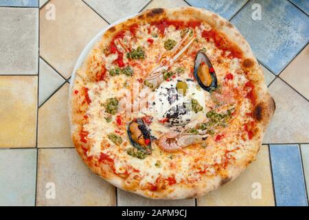 Köstliche Meeresfrüchte-Pizza mit Garnelen und Muscheln auf einem farbenfrohen Tisch im Ljubljana Café, Slowenien Stockfoto