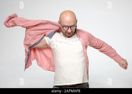 Kahler Mann mit Brille auf ein korallenfarbiges Hemd, er bereitet sich auf eine Veranstaltung vor und ist sehr ernst. Stockfoto