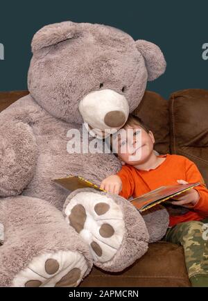 Junge kuscheln mit seinem Teddybären und einem guten Buch Stockfoto