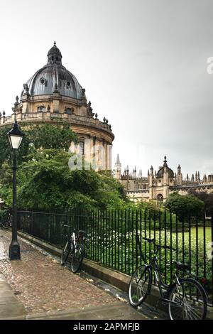 Radcliffe Camera und All Souls College an einem regnerischen Tag. Die Fahrräder ruhen auf einem Stachelmetallgeländer, das einen grünen Rasen umschließt. Straßenlaterne und gepflasterter Pfad. Stockfoto