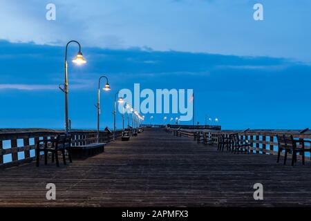 Ventura Pier, Blick auf den Seitenrand vor Sonnenaufgang. Gehweg verlassen; Lampen leuchten noch, blaue Wolken und Himmel im Hintergrund. Stockfoto