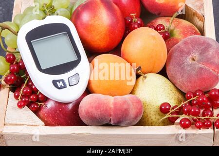 Glucometer Feind messen Blutzucker und frische Früchte in Holzkiste als gesunder Snack oder Dessert mit natürlichen Vitaminen und Mineralien Stockfoto