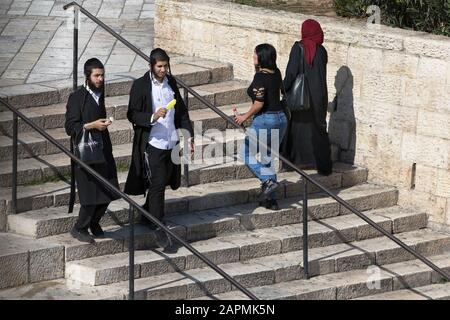 Fußgänger auf den Stufen, die zum Damaszener Tor der Altstadt von Jerusalem hinabgehen, mit zwei ultraorthodoxen jüdischen Männern, die Eis und Päpste essen Stockfoto