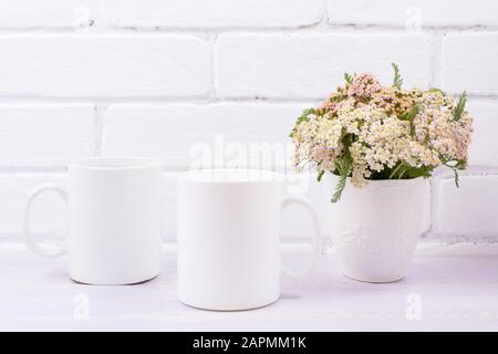 Zwei weiße Kaffeebecher mit rosa beigen Wildblumen in der Vase. Leerer Becher zum gestalten. Stockfoto