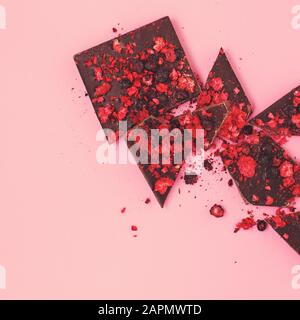 Zerkleinert auf Stücken schwarzer Schokoladenriegel mit verstreuten getrockneten roten Beeren auf pinkfarbenem Hintergrund, flachem Lay, Vintage instagram Farben Stockfoto