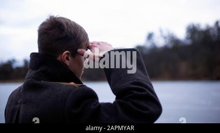 Marinesoldat Junior Leutnant in einem schwarzen Mantel trifft auf ein Schiff. Stockfoto