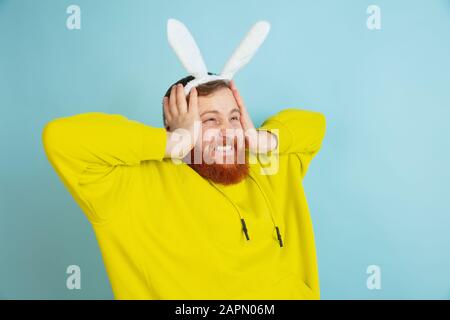 Schockiert, staunend. Kaukasischer Mann als Osterhase mit heller lässiger Kleidung auf blauem Studiohintergrund. Frohe ostergrüße. Konzept menschlicher Emotionen, Gesichtsausdruck, Feiertage. Copyspace. Stockfoto