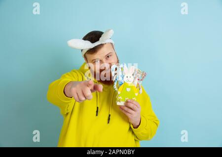 Zeigen, auswählen. Kaukasischer Mann als Osterhase mit heller lässiger Kleidung auf blauem Studiohintergrund. Frohe ostergrüße. Konzept menschlicher Emotionen, Gesichtsausdruck, Feiertage. Copyspace. Stockfoto