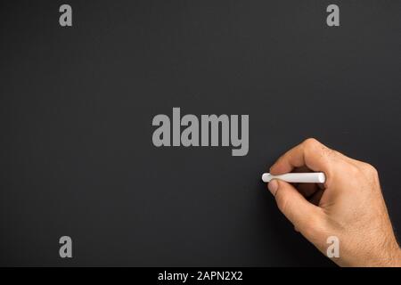 Nahaufnahme der Hand des Mannes, die Kreide gegen leere schwarze Tafel hält Stockfoto