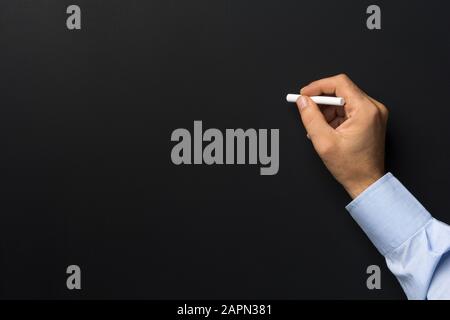 Nahaufnahme der Hand des Mannes, die Kreide gegen leere schwarze Tafel hält Stockfoto