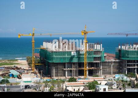 VIETNAM da NANG - April 10, 2019: Krane und Gebäude Baustelle gegen den blauen Himmel und das Meer. Metall Bau der unvollendete Gebäude auf Stockfoto