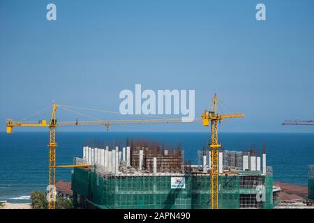 VIETNAM da NANG - April 10, 2019: Krane und Gebäude Baustelle gegen den blauen Himmel und das Meer. Metall Bau der unvollendete Gebäude auf Stockfoto