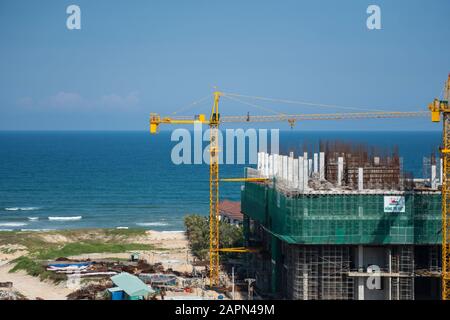 VIETNAM da NANG - April 10, 2019: Krane und Gebäude Baustelle gegen den blauen Himmel und das Meer. Metall Bau der unvollendete Gebäude auf Stockfoto