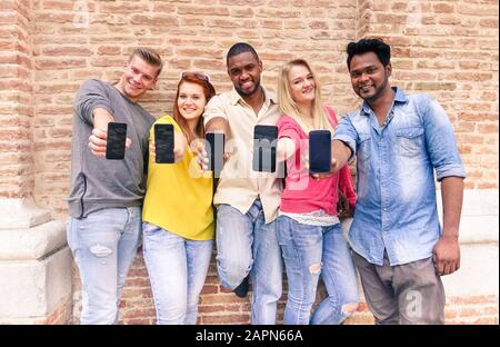 Multirassische Freundesgruppe, die im Freien leere Smartphone-Bildschirme zeigt - Junge multiethnische Menschen haben Spaß mit Mobiltelefonen - technologiesüchtig Stockfoto