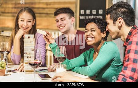 Junge Studenten spielen Brettspiel im Wohnzimmer der Jugendherberge - Verschiedene Kulturleute, die Spaß haben und Wein im Pub-Restaurant trinken - Freundschaft und Alter Stockfoto