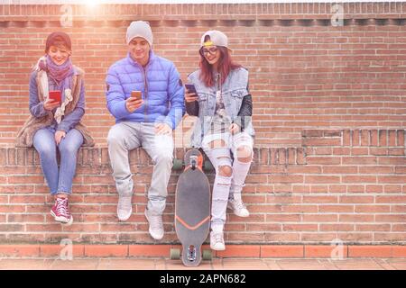 Gruppe junger Freunde, die online mit Smartphones im Freien spielen - Fröhliche Trend-Leute sind abhängig vom mobilen - Technologie- und Modekonzept in der Stadt Stockfoto