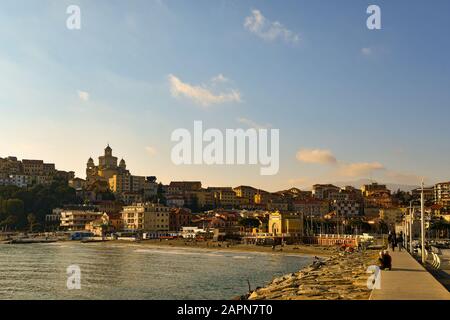 Blick auf die Bucht vom Kai des Hafenviertels mit dem Stadtteil Parasio auf dem Vorgebirge über dem Sandstrand, Porto Maurizio, Imperia, Ligurien, Italien Stockfoto