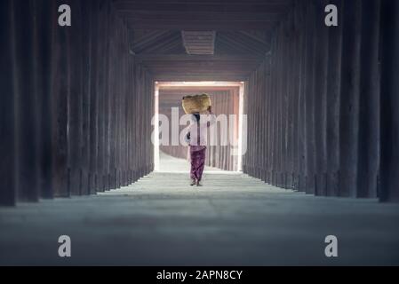 Frau läuft auf dem Gehweg mit Körben auf dem Kopf im Tempel, in der nördlichen Region von Myanmar, Myanmar Stockfoto