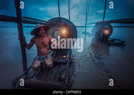 Asiatischer Fischer hält eine Laterne auf seinem Boot und wartet auf Fische im Mekong. Während der Dämmerung Stockfoto