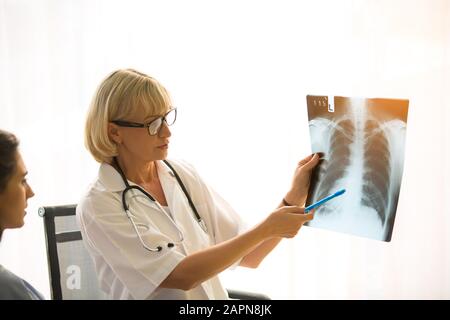 Der Arzt erklärt den Patienten in der Klinik oder Im Arzt des Büros, der ein Röntgenbild untersucht und mit einem Patienten diskutiert, den Röntgenstrahl der Lunge Stockfoto