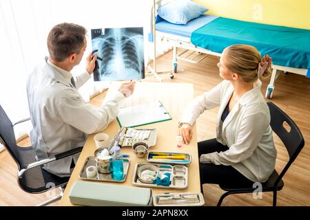 Der Arzt erklärt den Patienten in der Klinik oder Im Arzt des Büros, der ein Röntgenbild untersucht und mit einem Patienten diskutiert, den Röntgenstrahl der Lunge Stockfoto