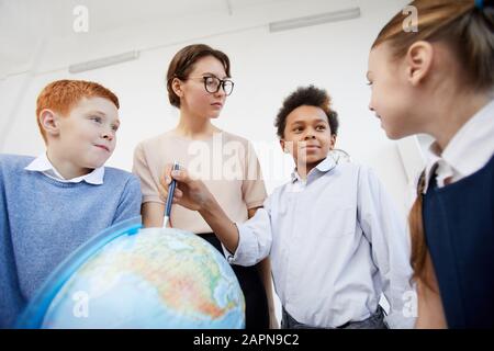 Afrikanischer Schuljunge, der auf die Weltkugel zeigt und seinen Klassenkameraden und Lehrern während des Unterrichts in der Schule von Ländern erzählt Stockfoto