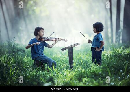 Kleines asiatisches Kind, das im Freien Geige spielt Stockfoto