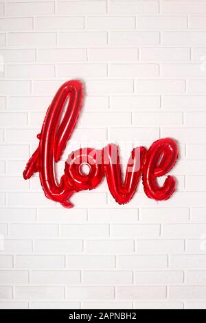 Roter Ball in Form des Wortes Liebe zu Rot an einer weißen Ziegelwand am Valentinstag. Stockfoto
