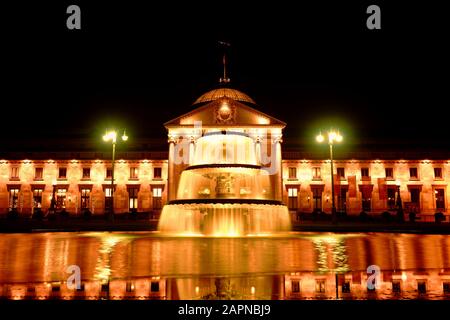 Wiesbaden, Deutschland: Kurhaus Kurhaus Casino und Springbrunnen nachts beleuchtet. Goldene Nachtszene mit Spiegelung im Wasser, hohe Auflösung. Stockfoto