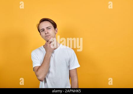 Weißer brünette Mann mit gelbem Hintergrund und weißem T-Shirt zeigt auf seinem Gesicht Finger auf Akne Stockfoto