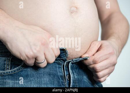 Mann mit großem Bauch knopt seine Hose kaum hoch. Stockfoto