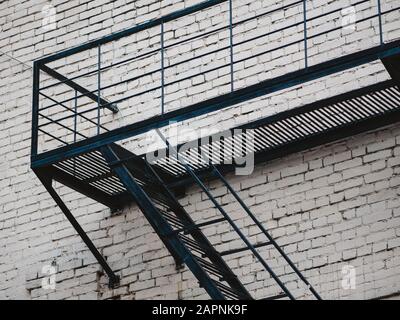 Fassade mit Feuerwehr-Stahlleiter des alten Hauses in Moskau, Russland. Das Feuer entweicht aus Stahlmetalarbeiten an der alten weißen Ziegelwand des Gebäudes. Exterio Stockfoto